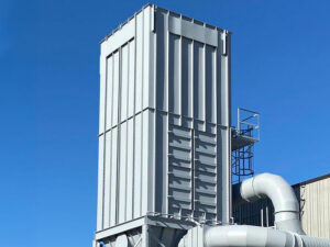 Tall corrugated metal exhaust/tower structure with attached large white ductwork, under a clear blue sky at an industrial facility