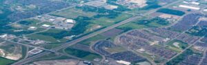 Aerial view of a highway interchange cutting through a suburban area with residential neighborhoods and green fields.