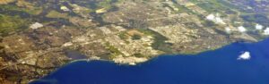 Aerial view of a coastal city with a harbor, dense housing, and grid-like streets along the shoreline.