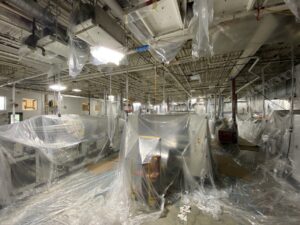 Industrial plant floor with equipment wrapped in plastic sheeting for painting prep.
