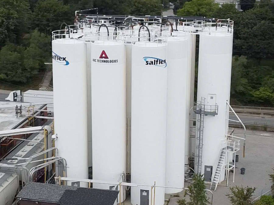 Industrial storage tanks with safety railings and ladders; logos for Salflex and AC Technologies visible on the white vertical tanks in an industrial facility.