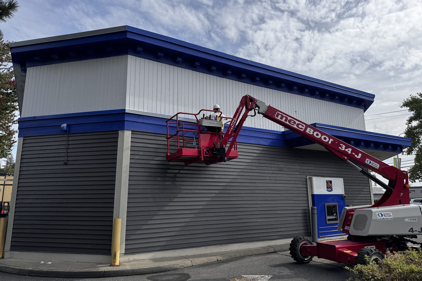 Painter on a boom lift painting the blue trim of a commercial bank building