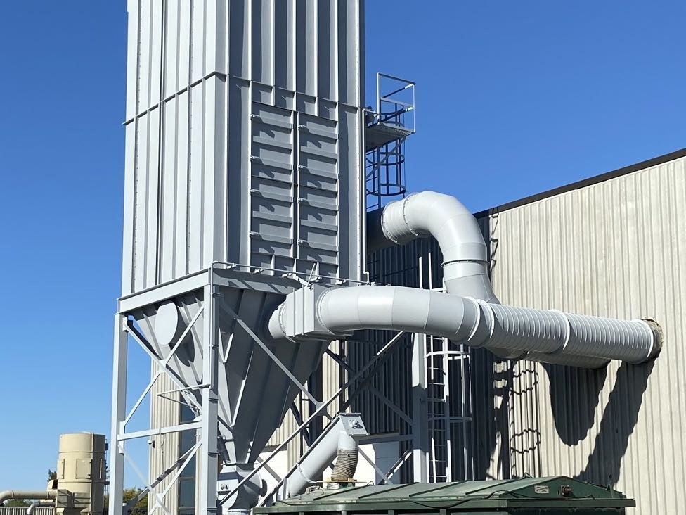 Grey industrial dust collector on a steel support frame above a green collection bin