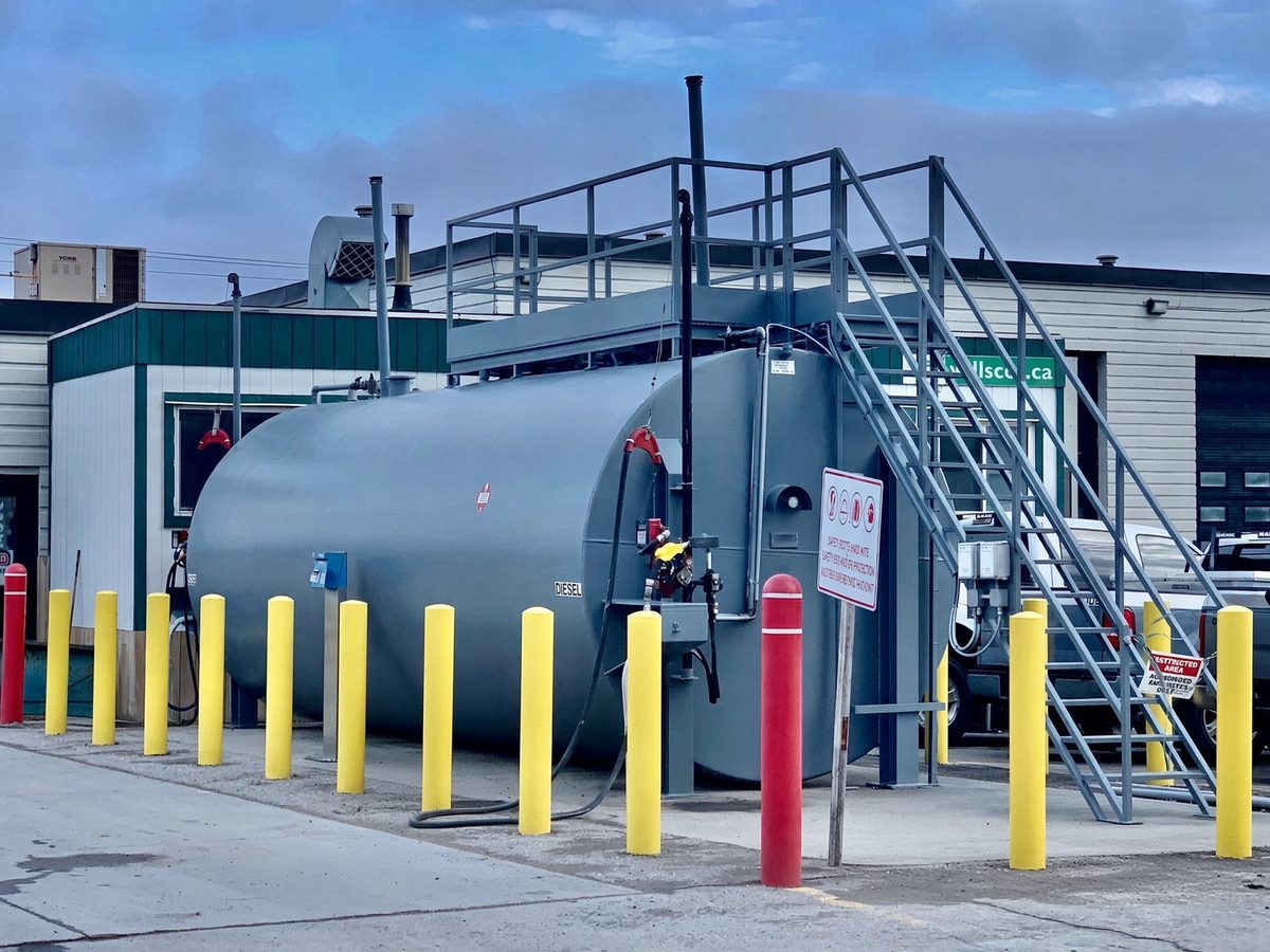 Grey above-ground diesel fuel tank with dispensing hardware, stairs and yellow safety bollards